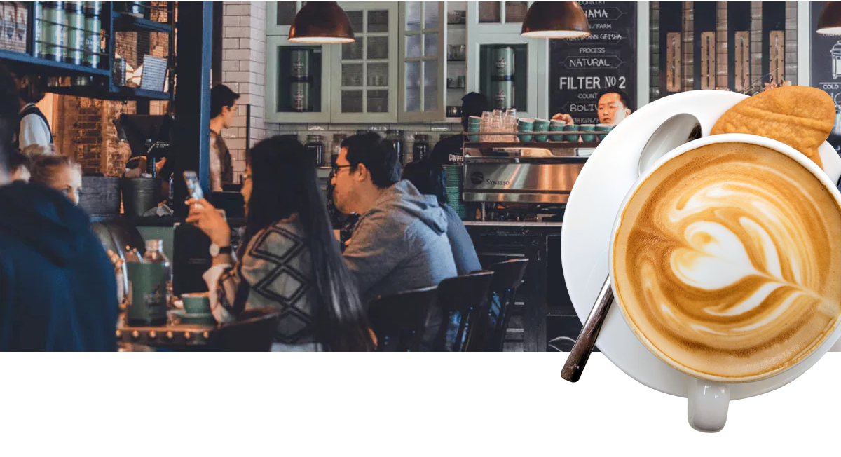 Customers sit chatting in a local coffee shop, lit wiht warm lighting.